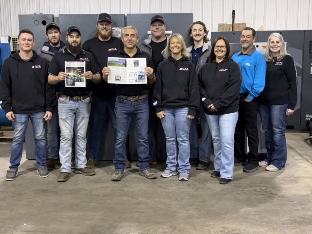 11 of Industrial Pneumatic Systems' employees standing in a group with two men holding up copies of the Compressed Air Best Practices magazine
